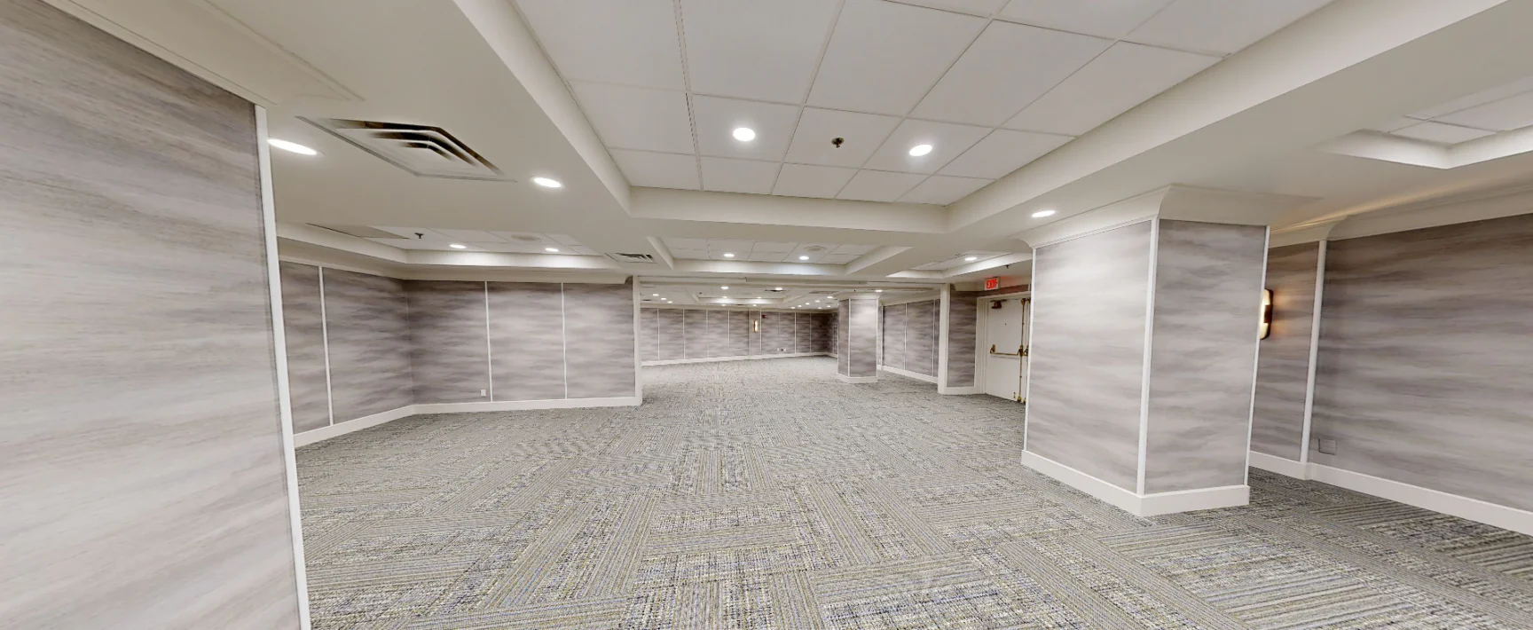 Spacious, empty conference room with gray carpet, light gray walls, recessed lighting, and a low, white-paneled ceiling.