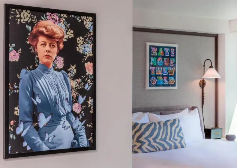 A modern bedroom with a bed, a zigzag pillow, a wall lamp, and two framed artworks, one featuring a woman in blue surrounded by flowers and butterflies.