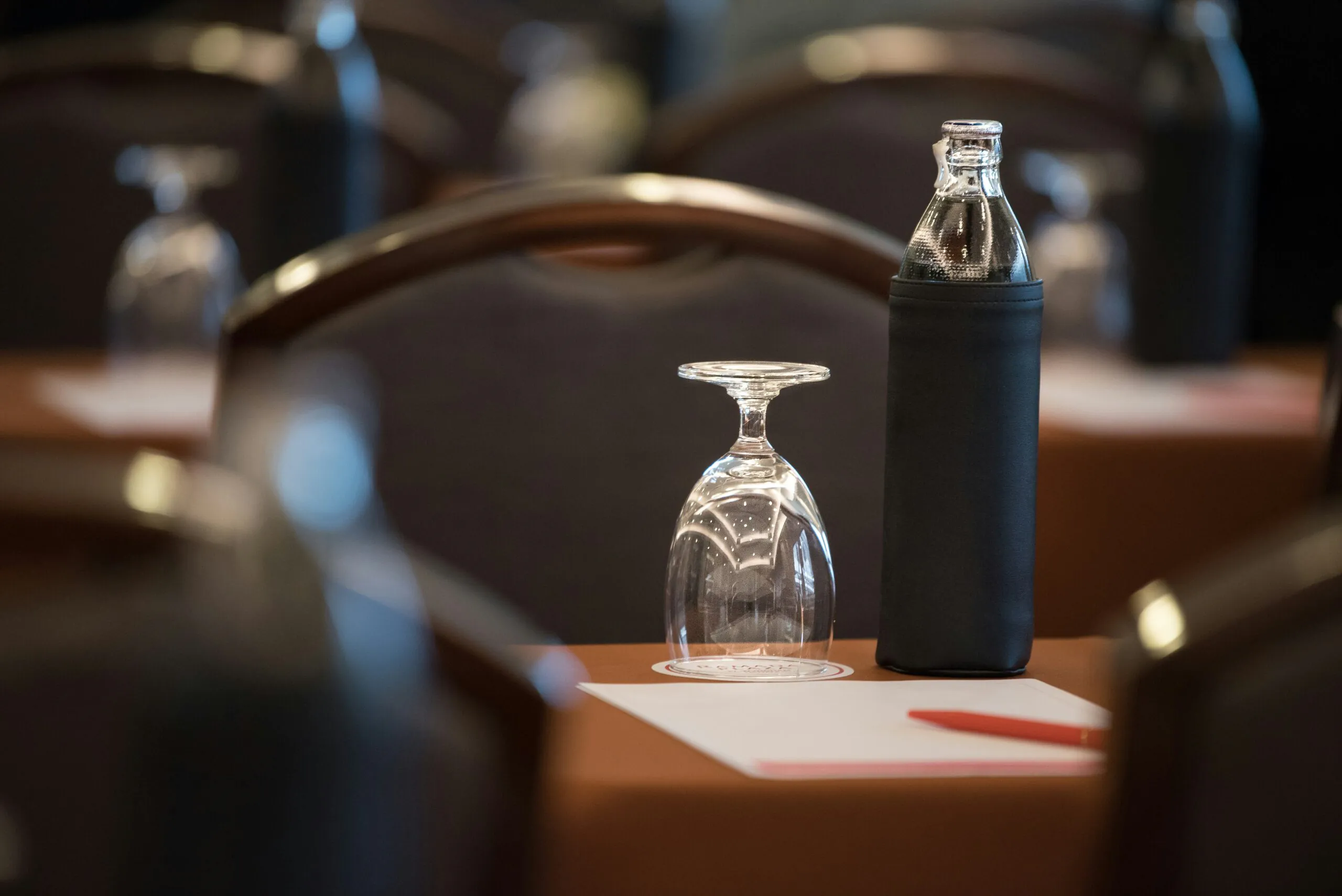 A glass and a bottled water on a table with a notepad and red pen, set up for a conference or meeting.